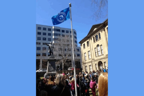 A town square filled with people and a Gaelic flag on a flagpole.