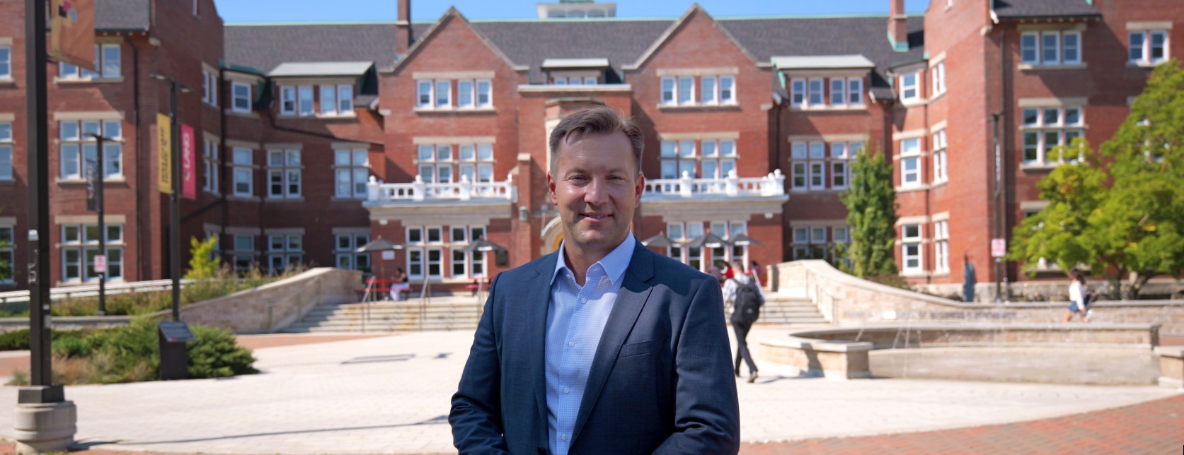 a person in white shirt and navy blue blazer poses in front of a red brick building