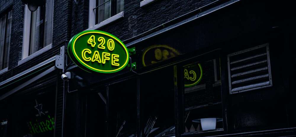 Green neon sign '420 Cafe' on a building facade in Amsterdam, creating a vibrant city atmosphere.