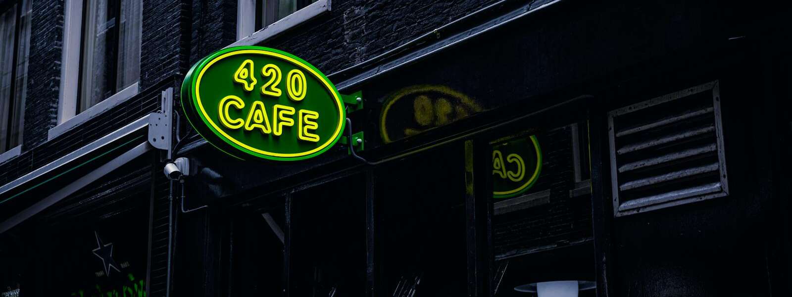 Green neon sign '420 Cafe' on a building facade in Amsterdam, creating a vibrant city atmosphere.