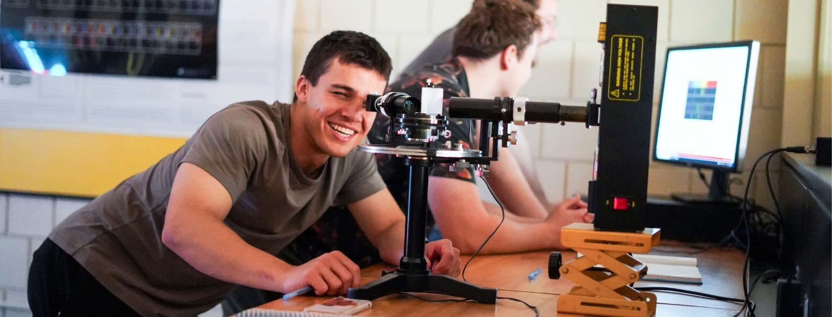 Student leans over to observe through a microscope at desk