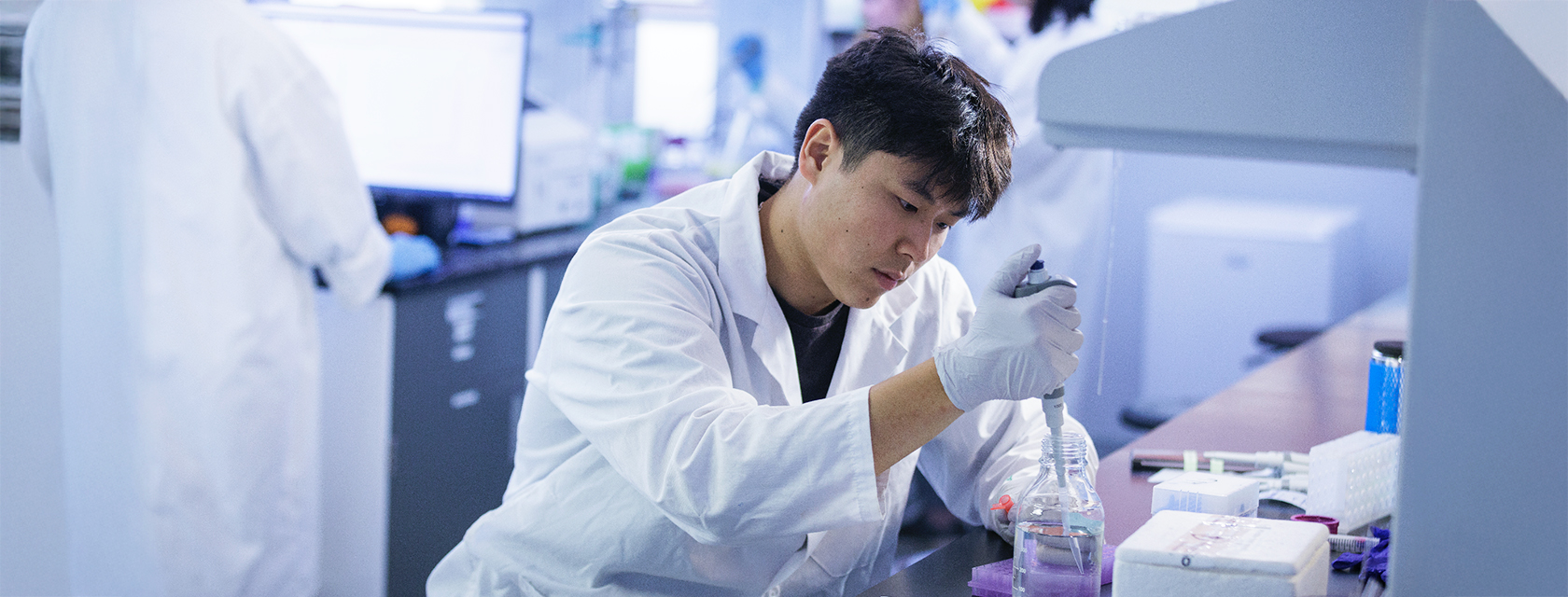 Student researcher in lab coat uses pipette at lab bench