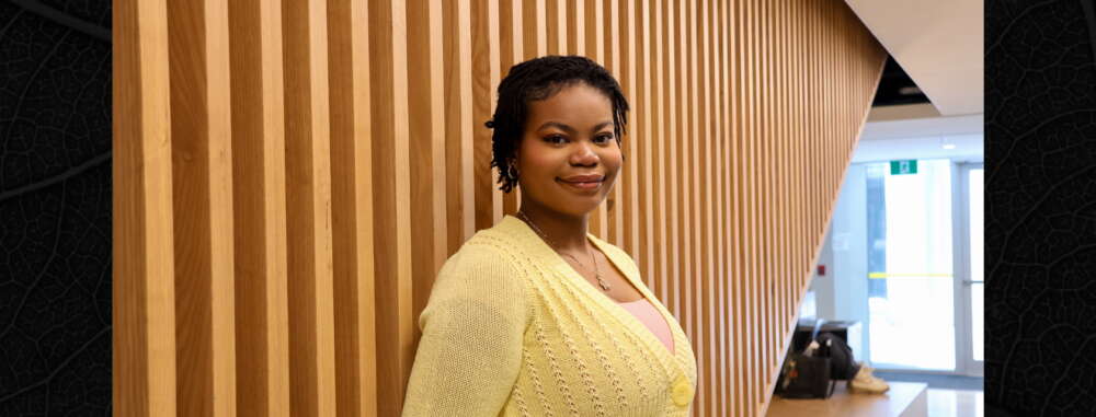 Ethieoghena Iluebbey with short dark hair smiles into camera against a wooden panel background