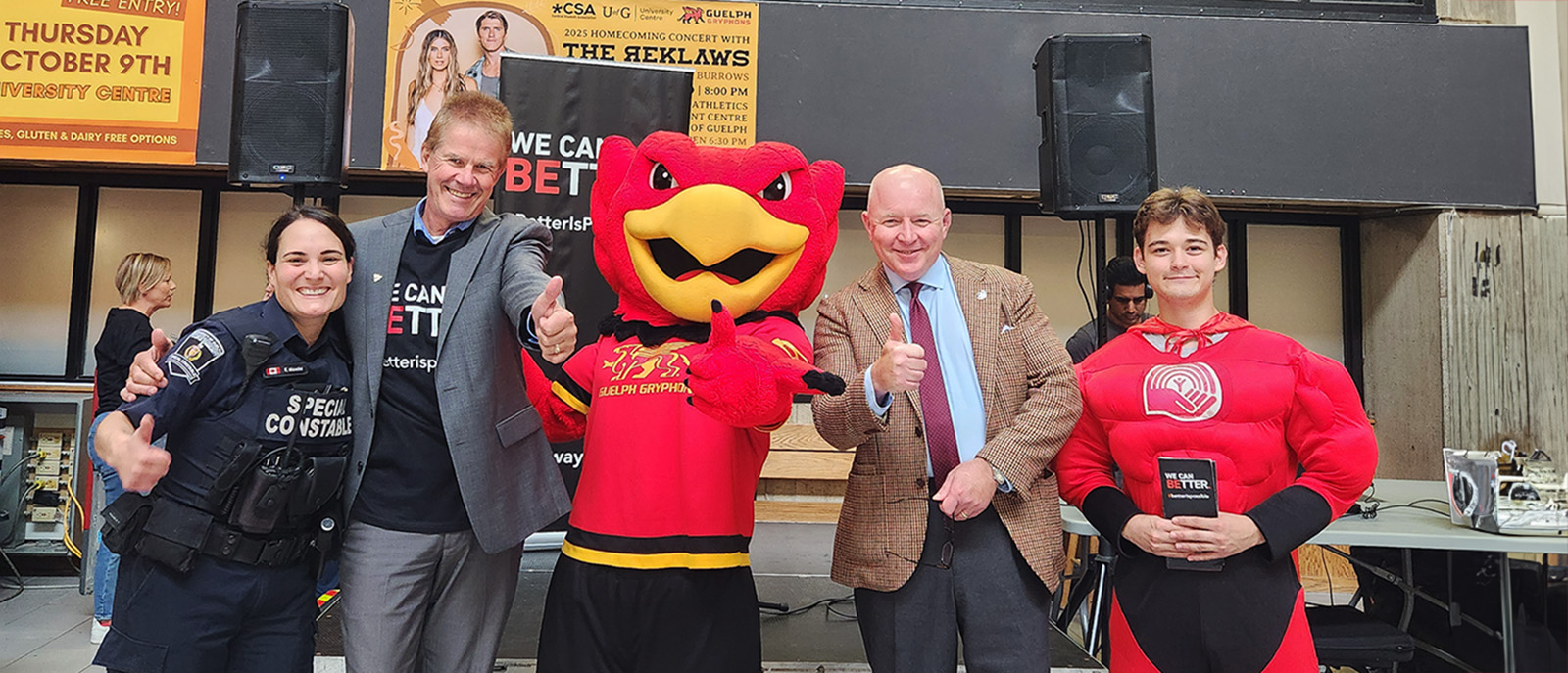 Four people stand around the Gryph mascot and give the thumbs up and smiles