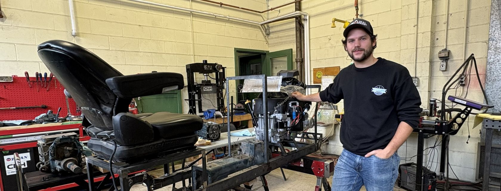 person stands beside a partially built tractor in an automotive shop