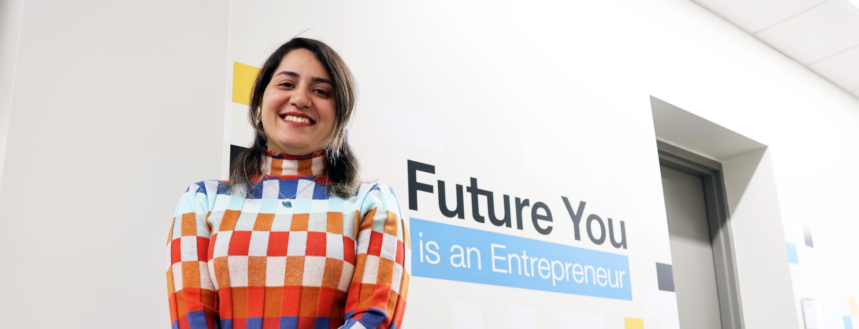 person in a patterned sweater stands in front of a white wall with the words "future you is an entrepreneur"